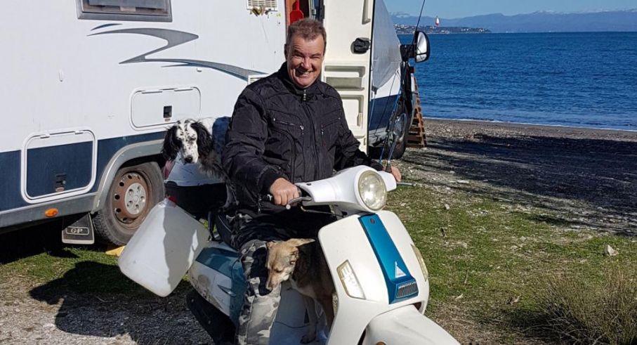 Peter Nyberg bor på heltid i sin husbil och har alltid fått bra vård när han blivit sjuk på sina resor. Man på vespa eller EU-moppe med hundar framför husbil och hav